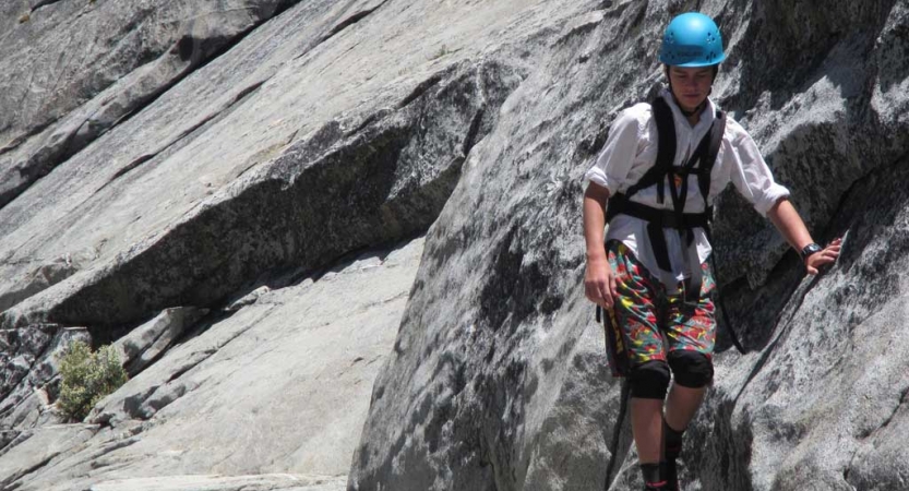 A person wearing saftey gear is secured by ropes as they navigate rocky terrain. 